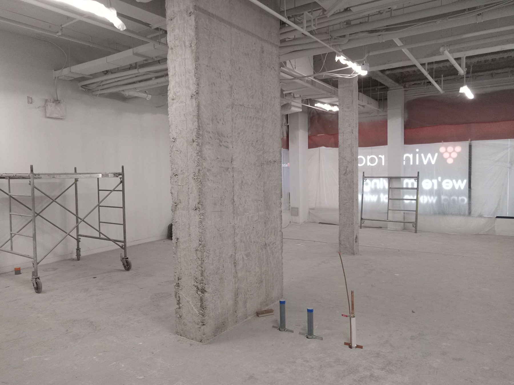Wine Rack space mid-construction: raw concrete columns, exposed ceiling and rough-in plumbing before fit-out